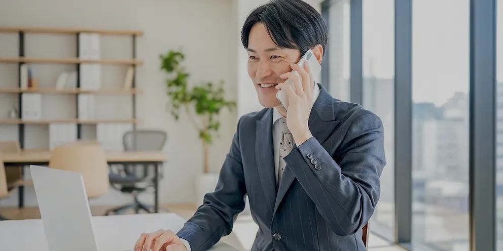 笑顔で電話対応をしながらパソコンを操作するスーツ姿の男性社員