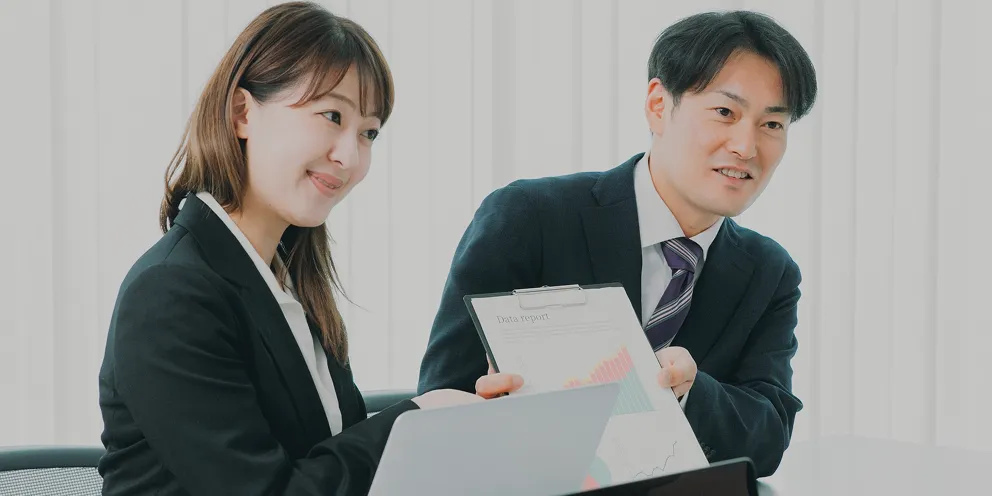 分析レポートを提示しながら成果を報告する、笑顔の男女コンサルタント