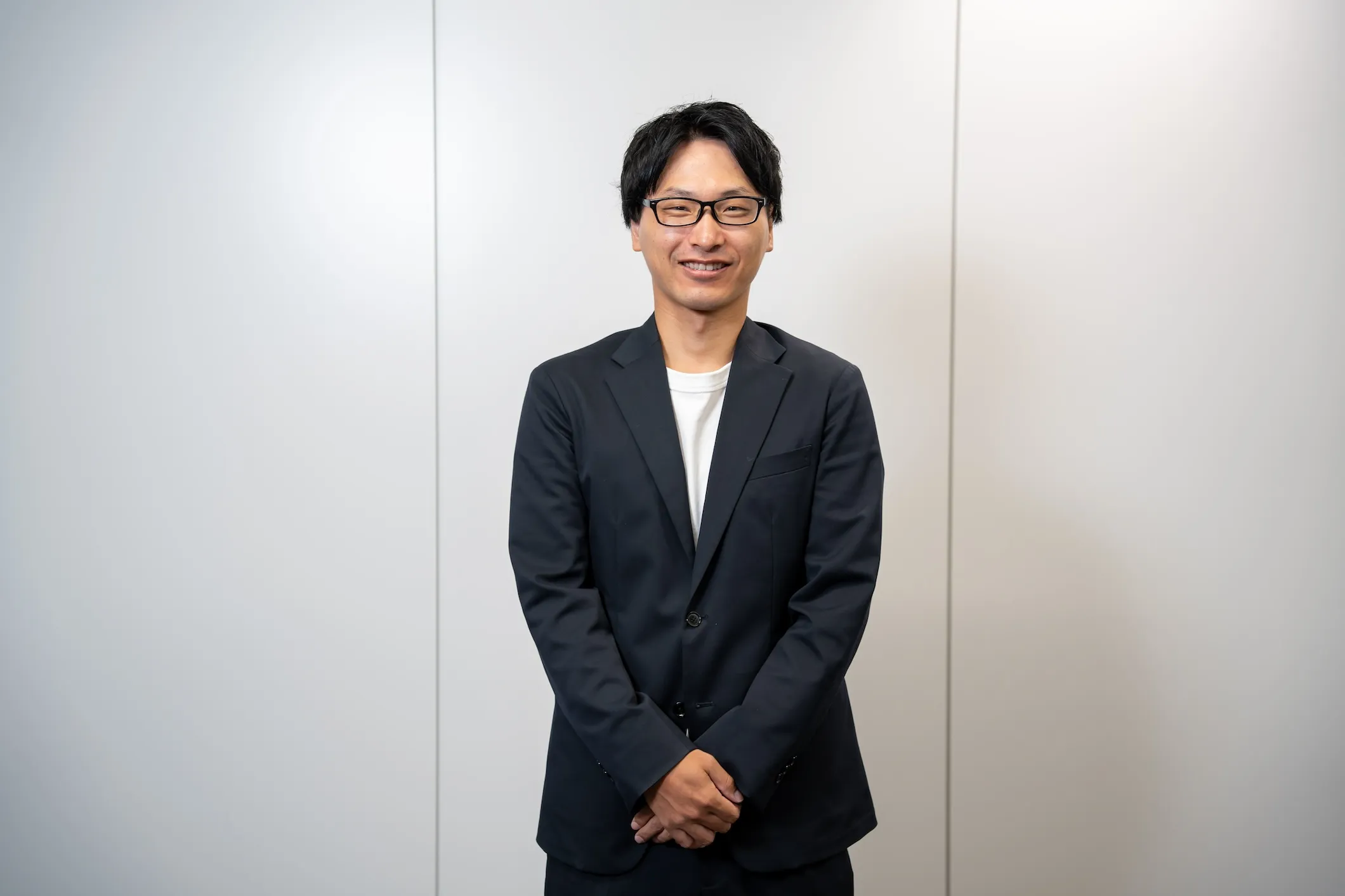 オフィスでジャケットを着用し、笑顔で立つ男性社員