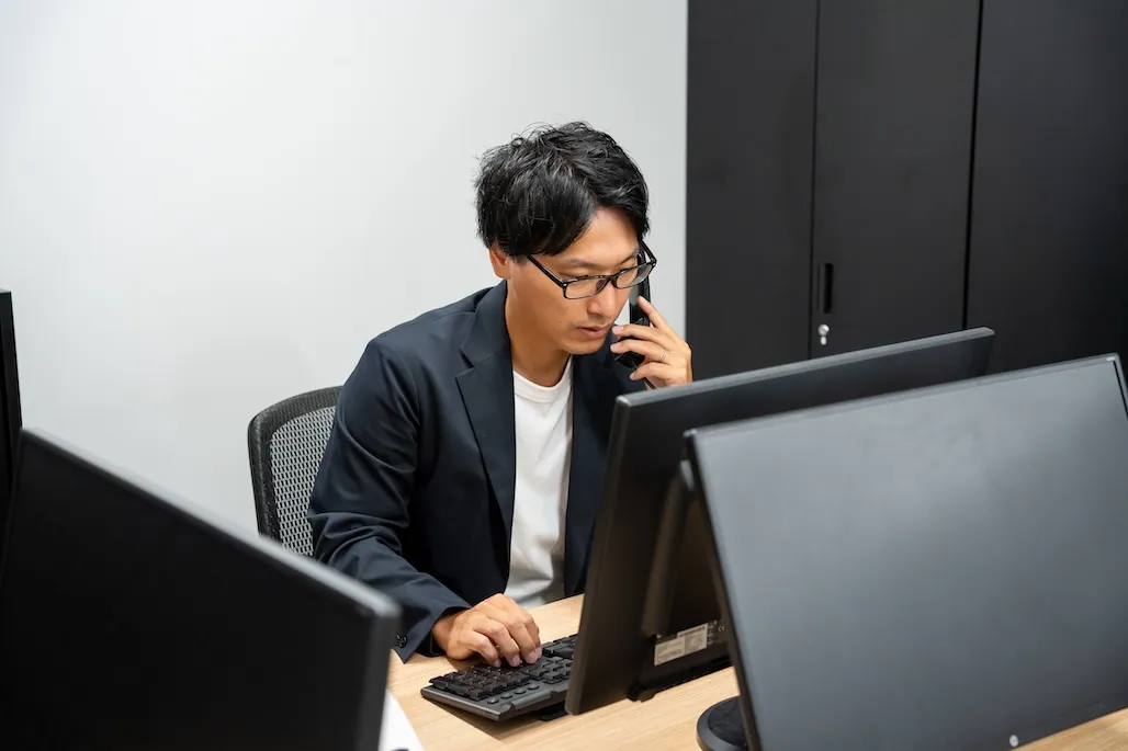 デスクでパソコンの画面を見ながら、電話対応をする男性社員
