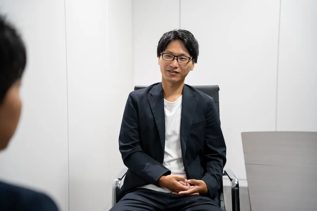 会議室の椅子に座り、他の社員と雑談をしている男性社員